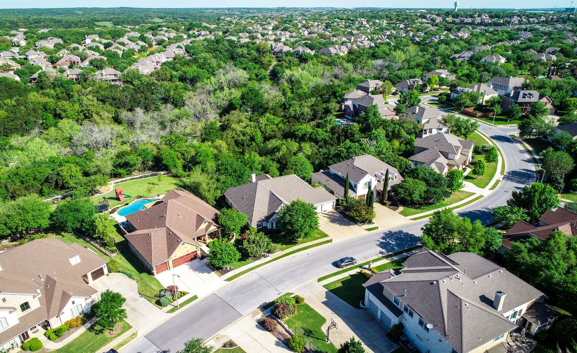 Aerial drone view above suburb homes in Cedar Park, Texas green Texas Hill Country landscape with large luxury homes and houses rooftops view high above landscape suburbs all the way to horizon