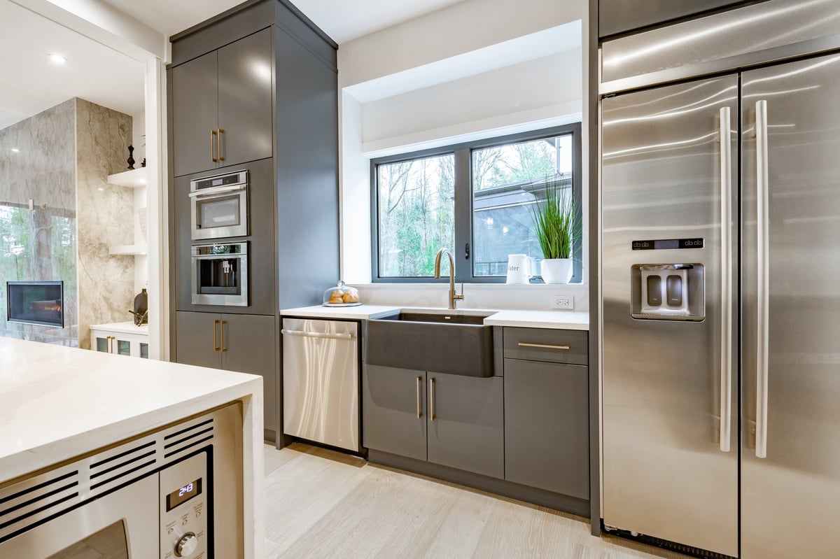 large and spacious kitchen with hardwood floors, stainless appliances, granite or marble countertops, grey cabinets and cupboards. Eating counter has bar stools and a dining area with chairs around the table. pendant lights hanging over the kitchen island, tile backsplash and built in ovens.