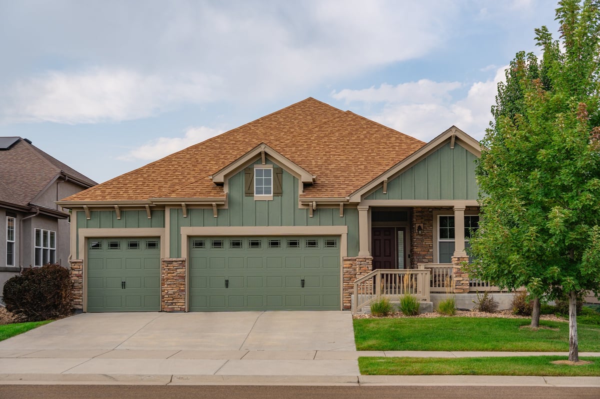 A newly constructed modern green wooden house in a suburban single-family neighborhood