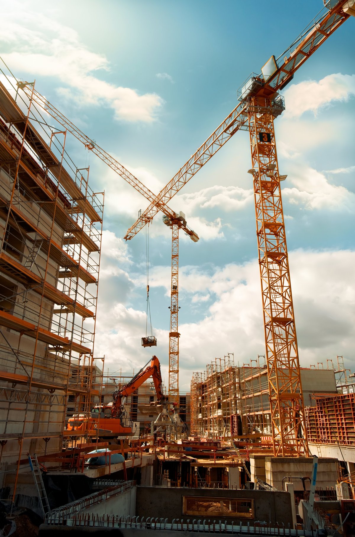 Construction site with yellow cranes looming into the blue sky with dramatic clouds.