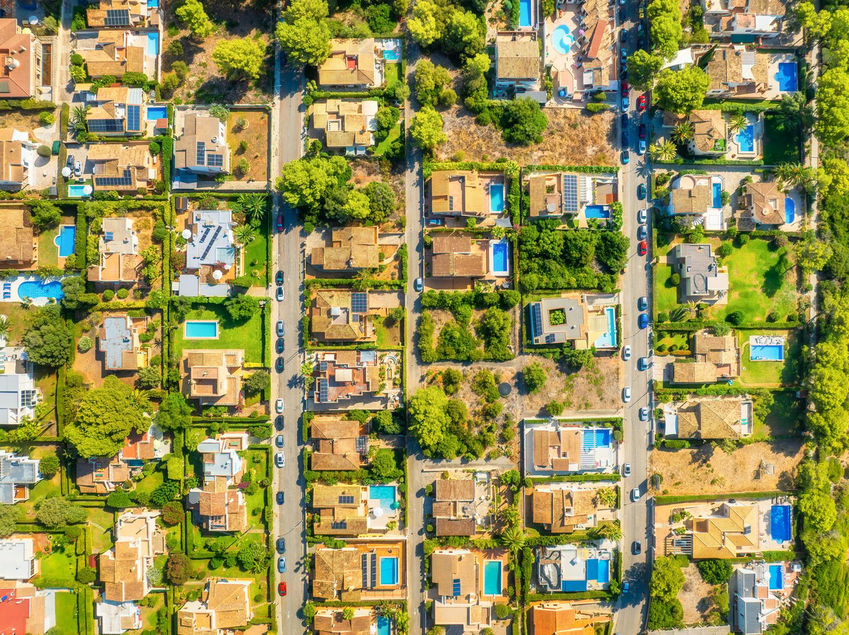 Aerial drone view of a modern residential neighborhood or resort area. Suburban streets with houses, hotel buildings, private swimming pools and people relaxing outdoors.