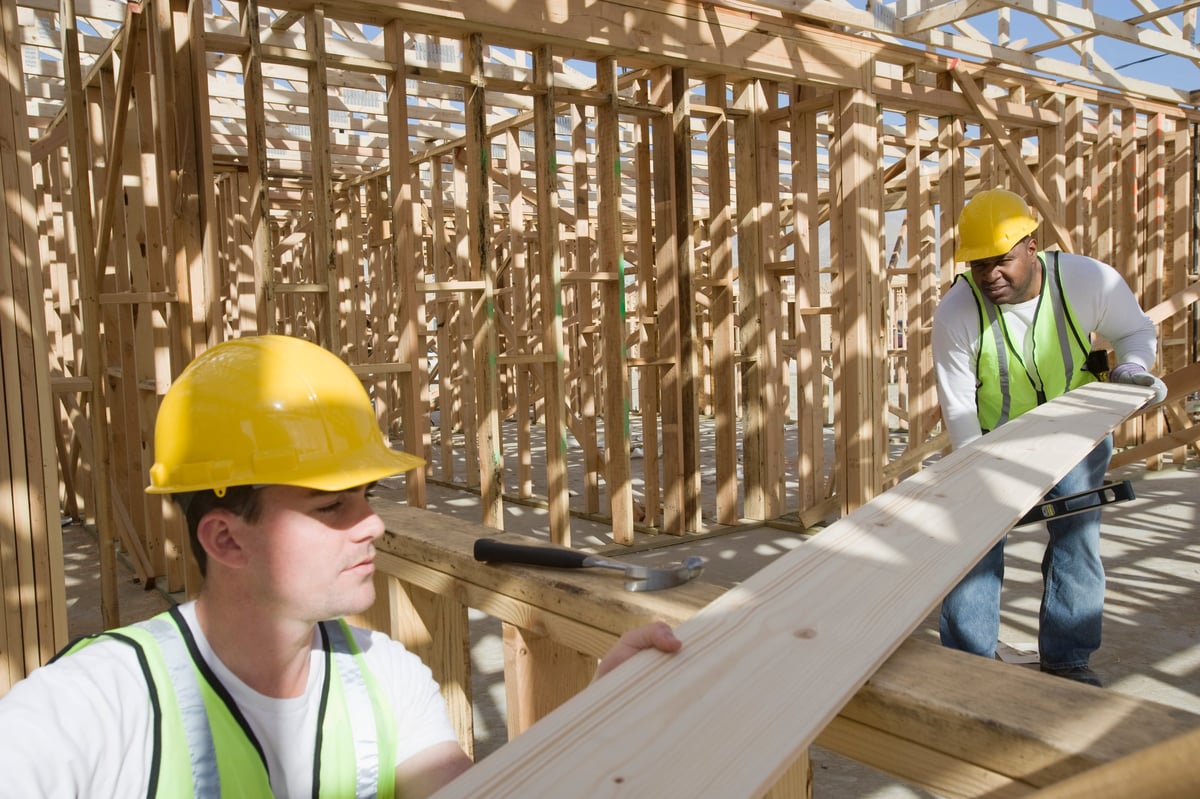 Two construction workers measuring wooden plank