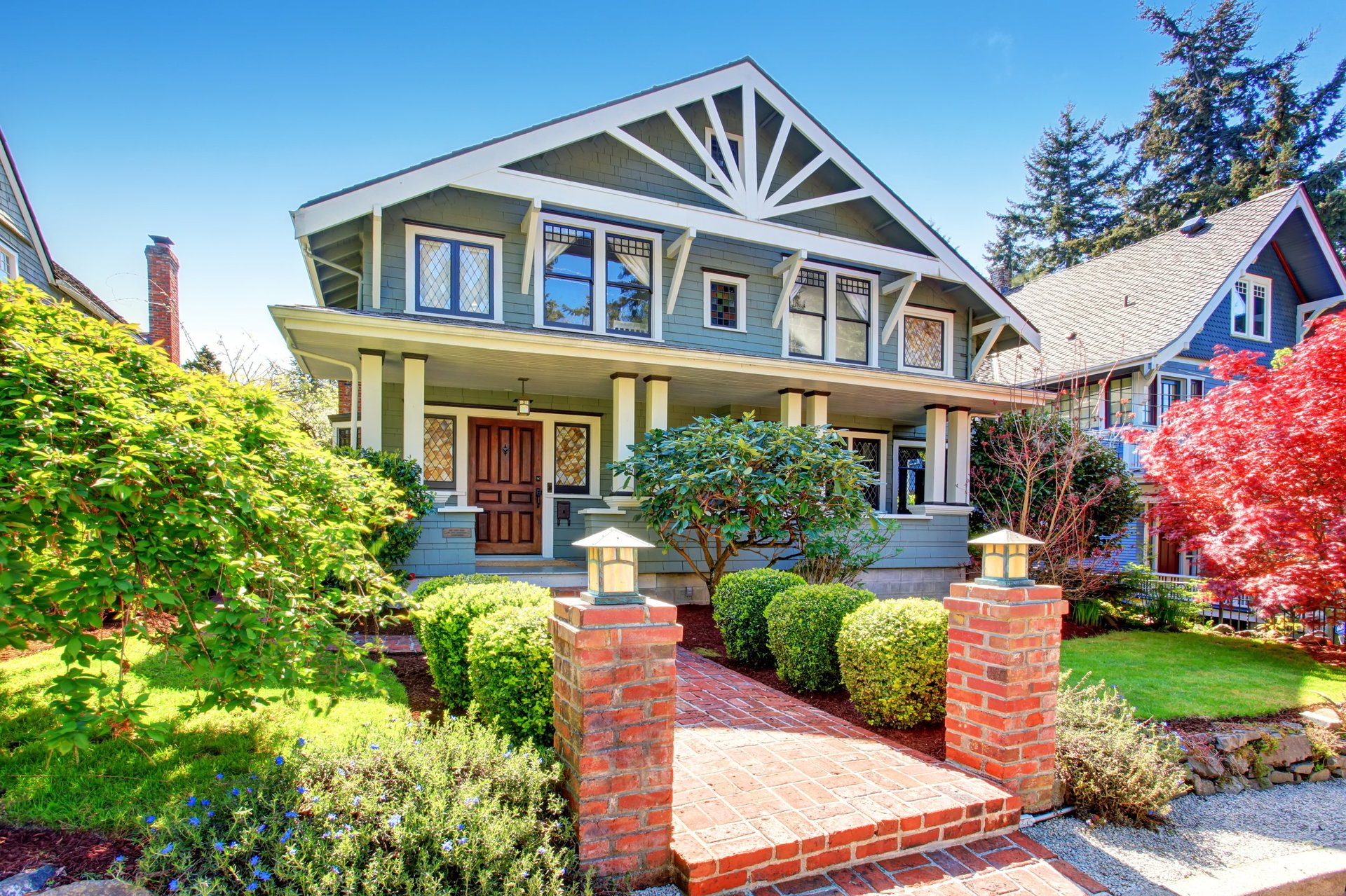 Large luxury blue craftsman classic American house exterior. View of brick walkway decorated with trimmed hedges.