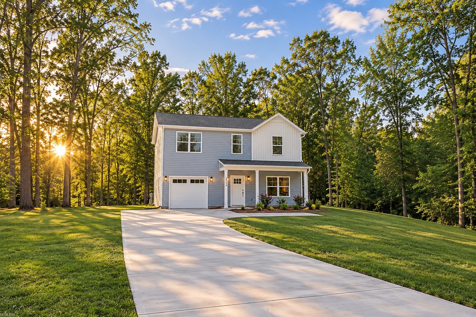 Modern two-story gray house with white trim, two-car garage, and concrete driveway set on manicured green lawn surrounded by trees at golden hour.