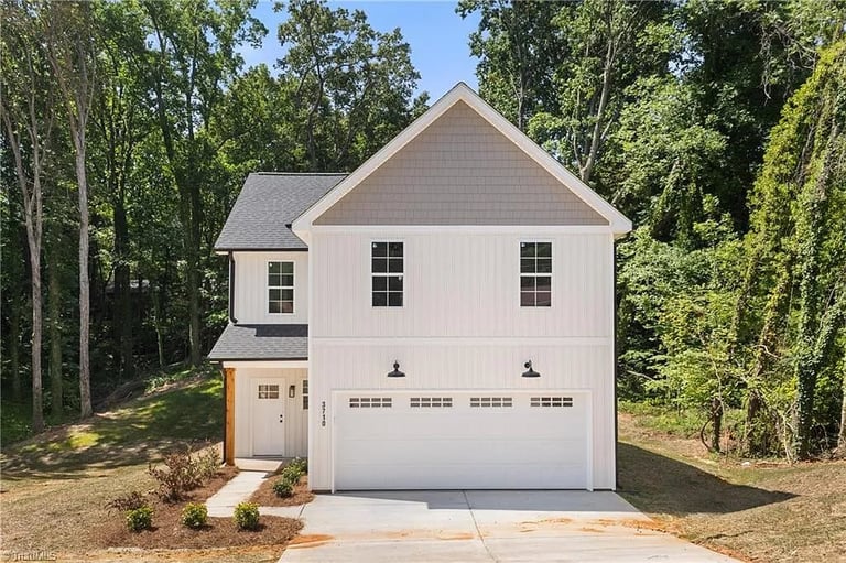 White two-story house with gray roof and three-car garage surrounded by tall trees and newly landscaped yard