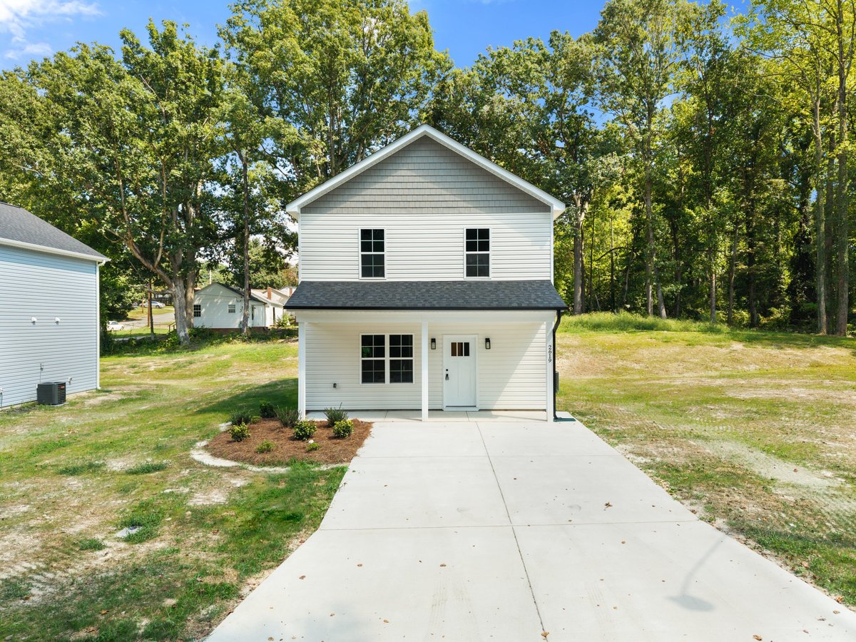 White two-story house with attached garage and concrete driveway, surrounded by tall trees and green lawn