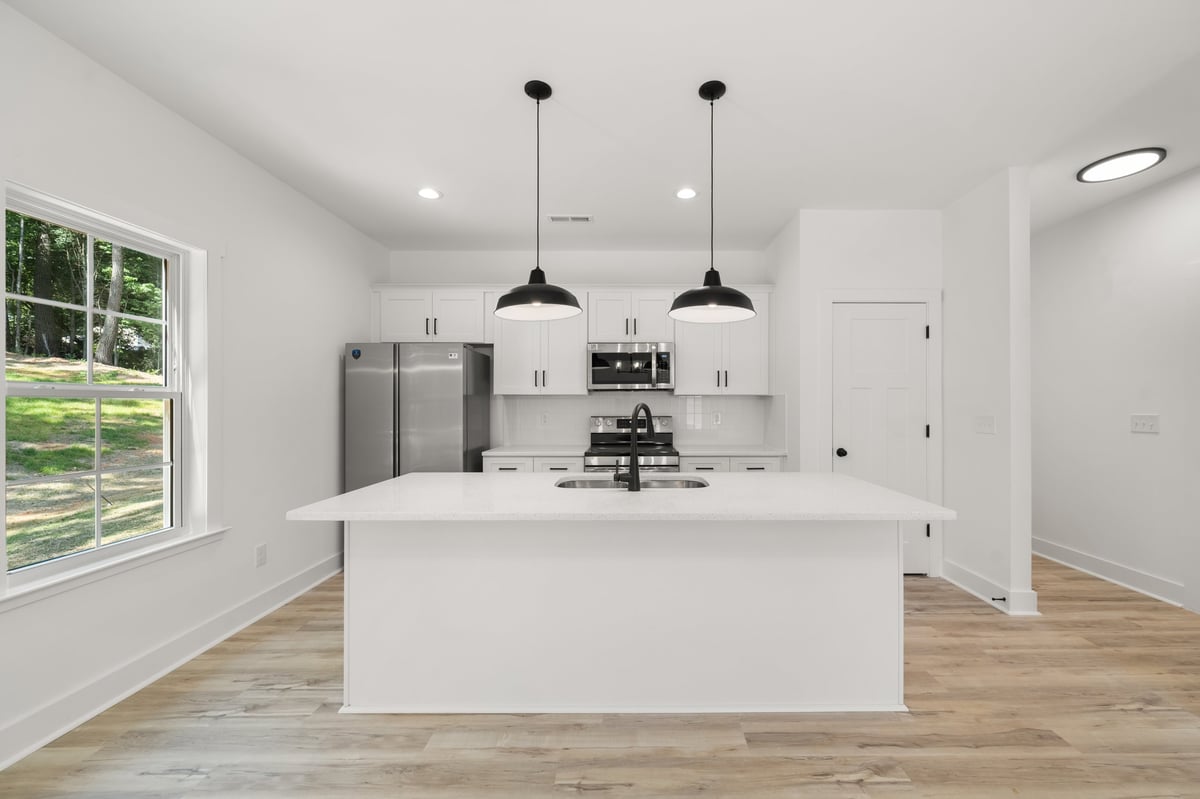 Modern kitchen with white island, stainless steel appliances, pendant lighting, and wood flooring