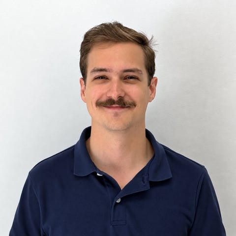 Man with brown hair and mustache wearing a dark blue polo shirt against a white background