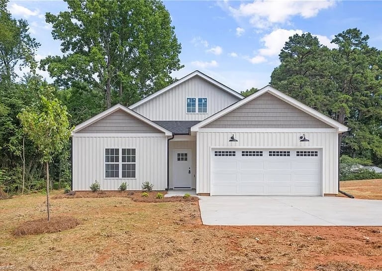 Completed LND Homes new construction white single-family home with two-car garage on a newly cleared lot surrounded by trees
