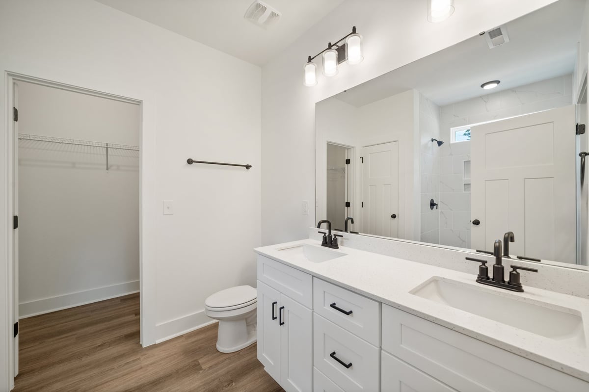 Modern white bathroom with double sink vanity, large mirror, toilet, and wood flooring