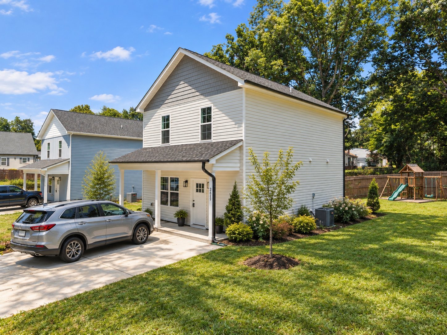 White two-story house with silver SUV parked in driveway, surrounded by green lawn and trees
