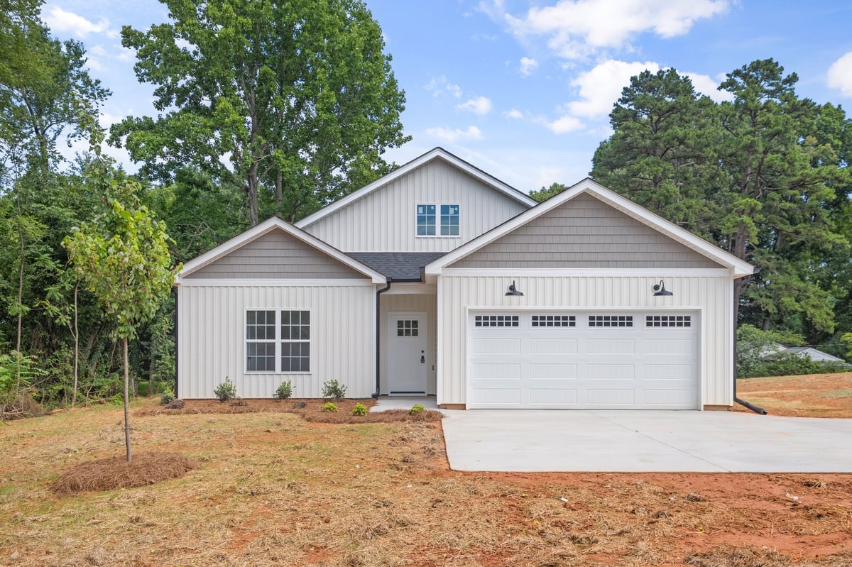Modern white farmhouse with two-car garage on newly cleared lot surrounded by mature trees