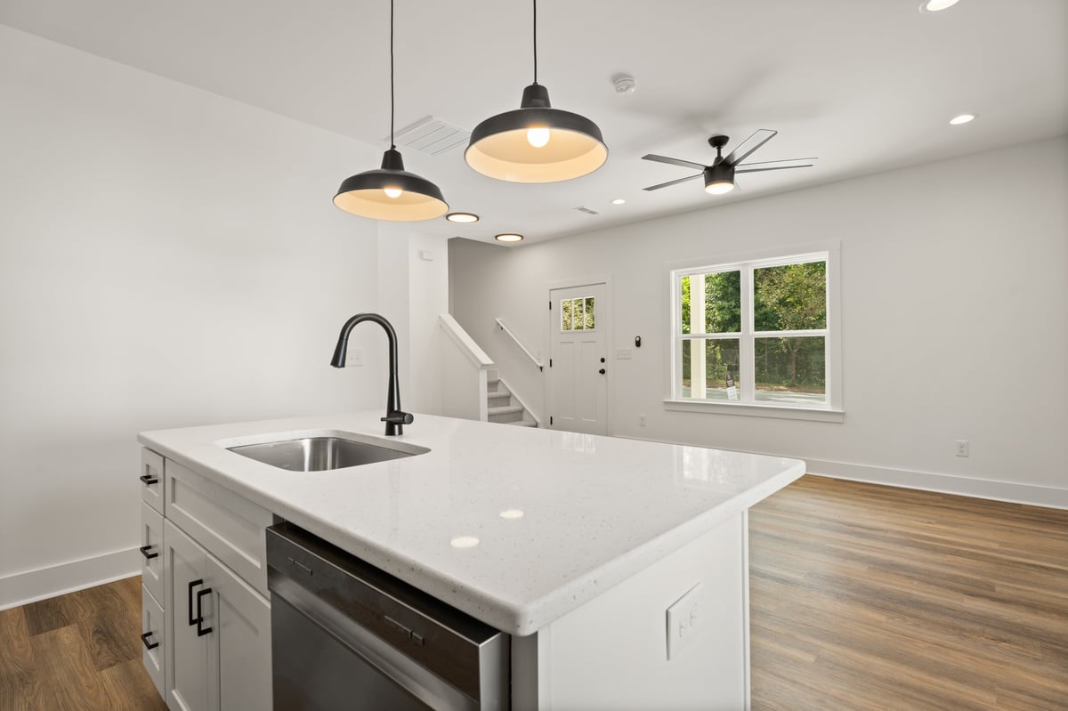 Modern kitchen with white island, pendant lights, stainless steel sink, built-in oven, and hardwood flooring.