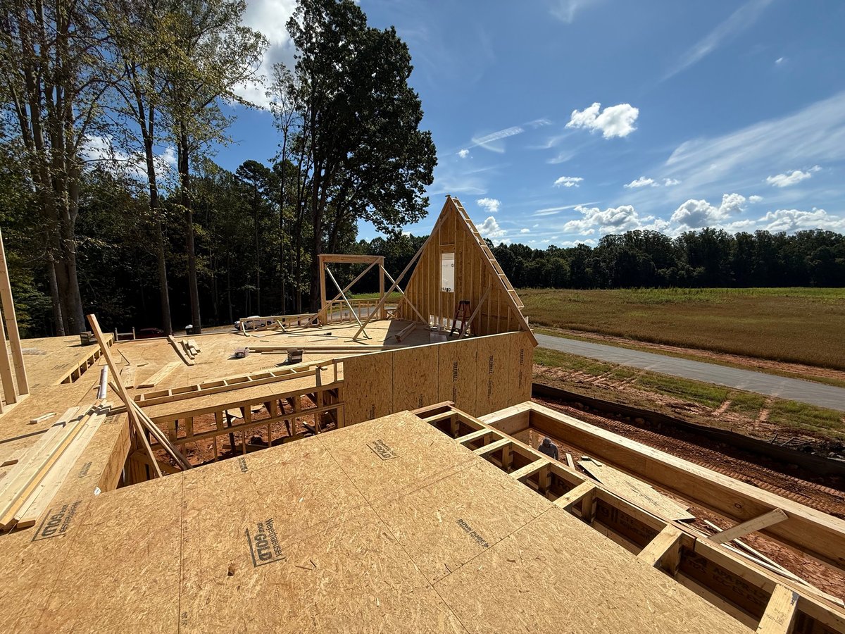 Construction site showing wooden framing of houses under development on rural property with trees and canal in background