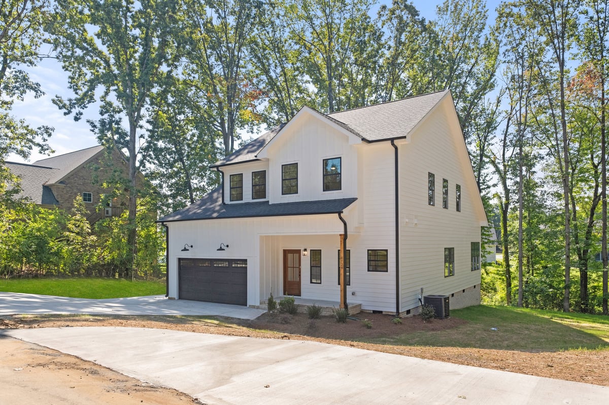 Modern two-story white house with dark roof, garage, and driveway surrounded by tall trees
