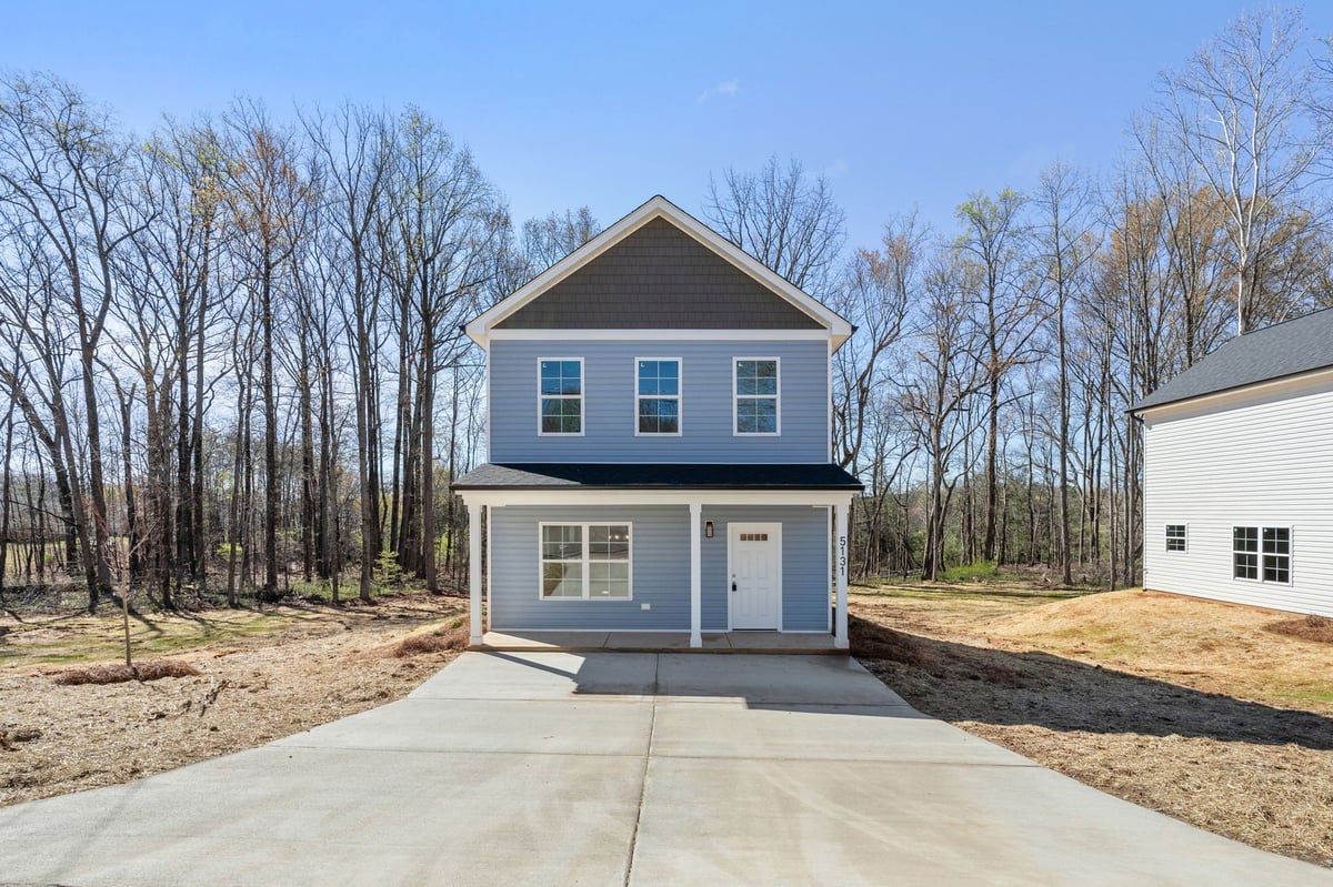 New two-story blue and white house on concrete driveway with bare trees and landscaping in suburban setting