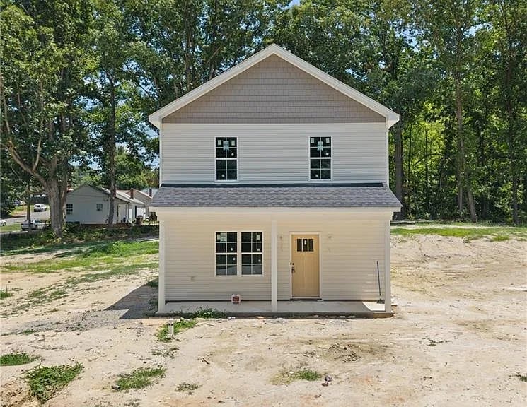 Two-story white house with beige trim, four windows, tan door, surrounded by trees on unpaved ground