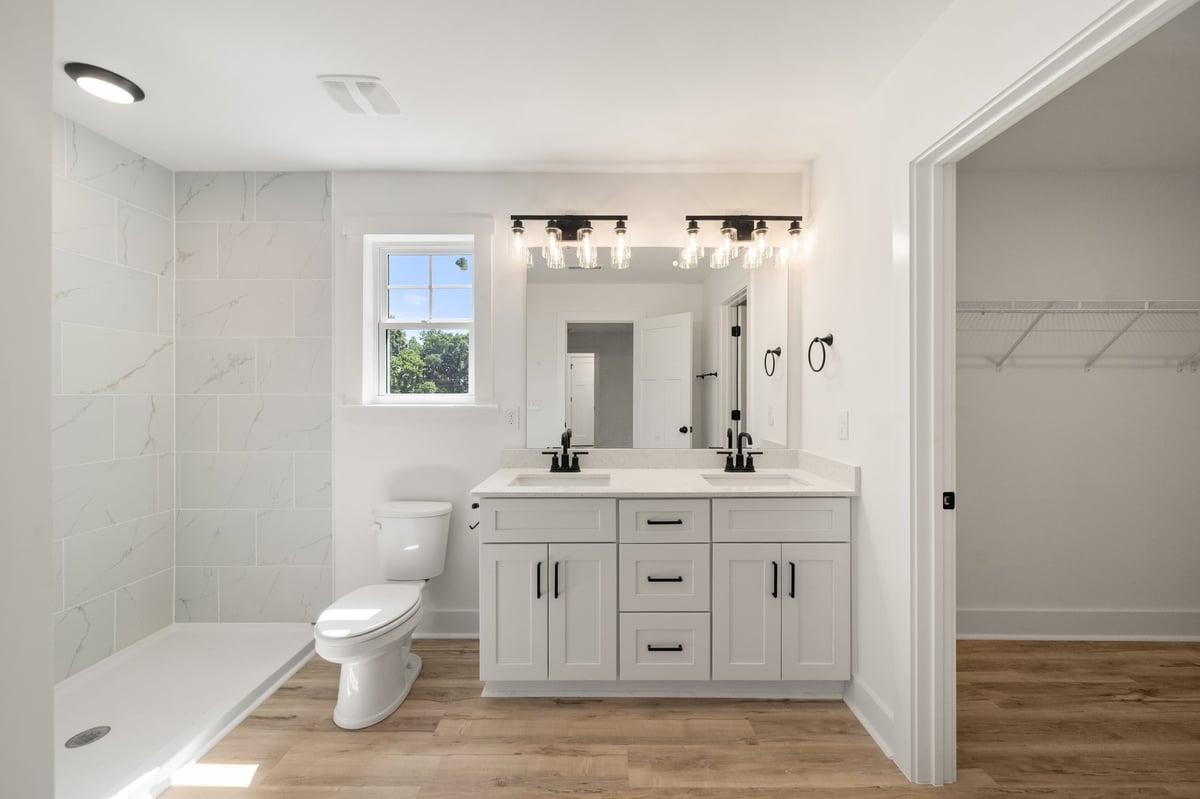 Modern bathroom with white vanity, double mirror, walk-in shower, toilet, and wood flooring