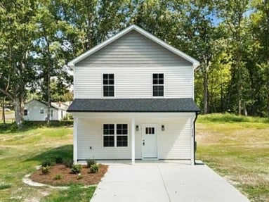 White two-story house with gray roof, front garage, and white doors surrounded by green lawn and trees