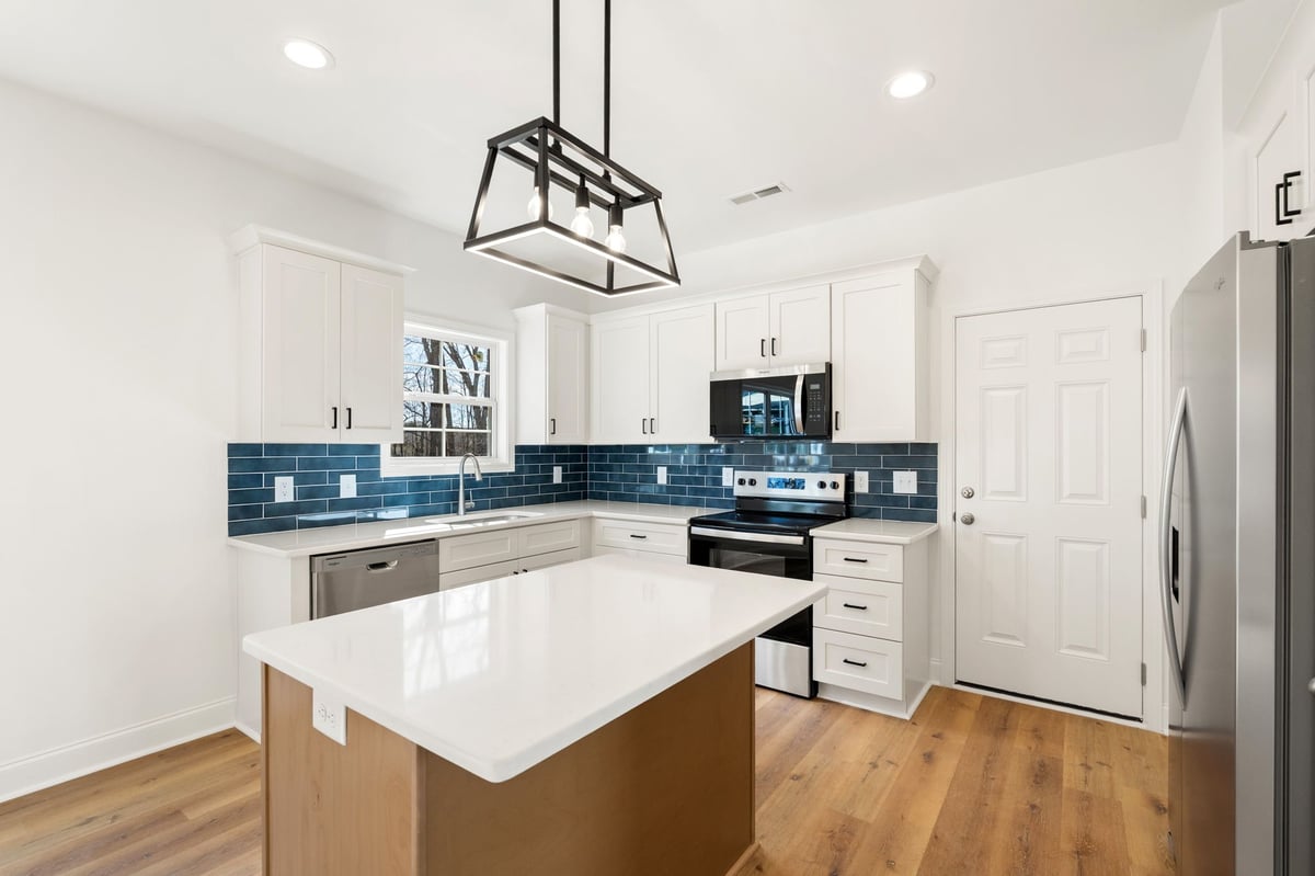 Modern kitchen with white and wood cabinetry, blue tile backsplash, white island countertop, stainless steel appliances, and hardwood flooring
