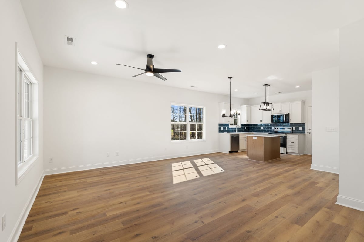 Modern open-concept kitchen and living area with hardwood floors, white walls, black ceiling fan, and navy blue kitchen cabinetry