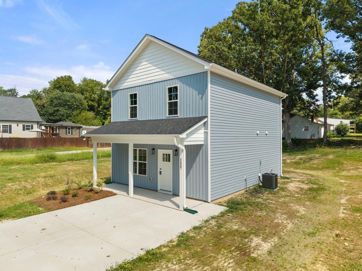 Modern two-story house with white siding, blue trim, and covered front porch on a residential lot surrounded by trees