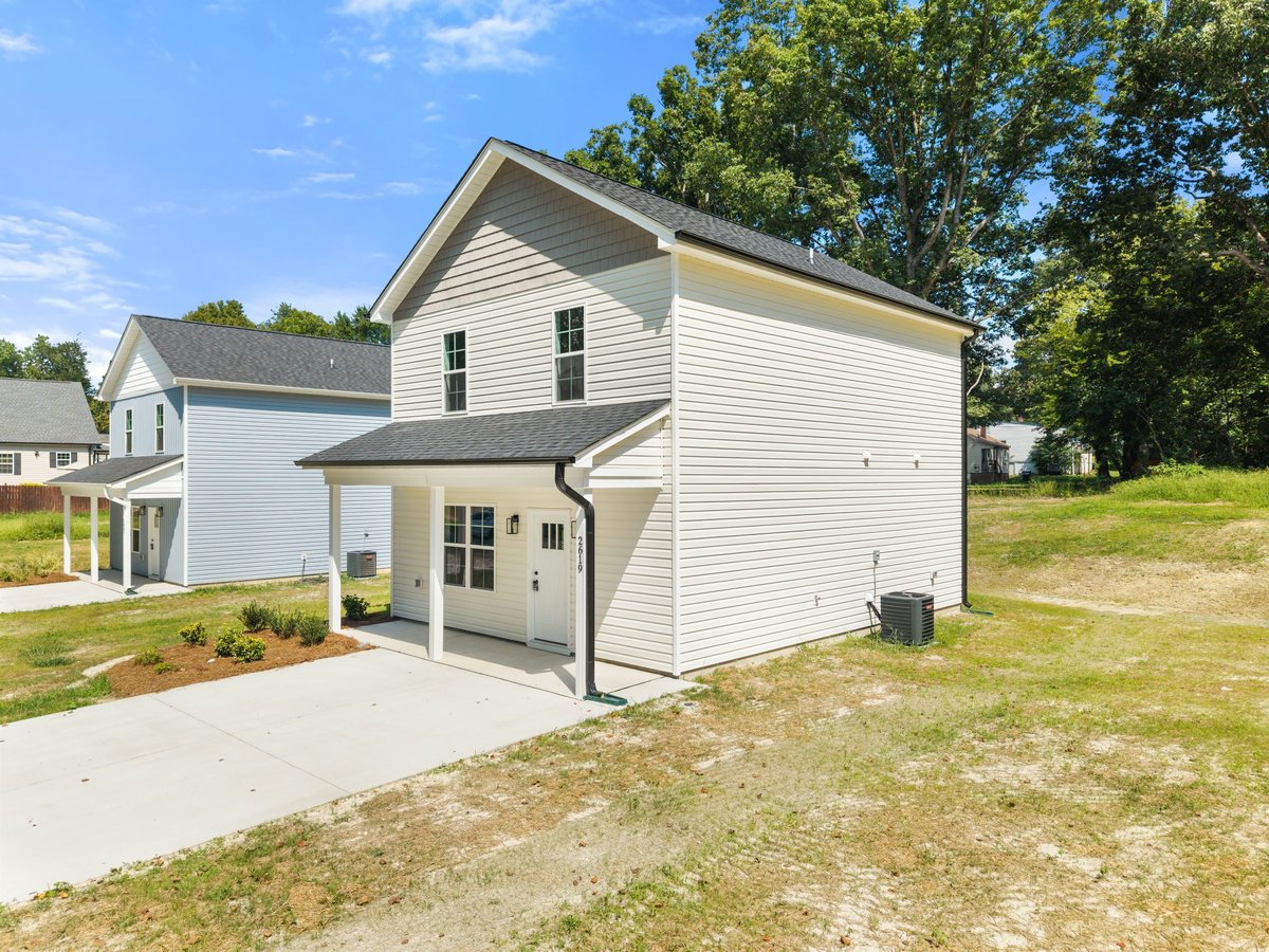 White residential two-story house with covered porch and attached garage on grassy lot surrounded by trees