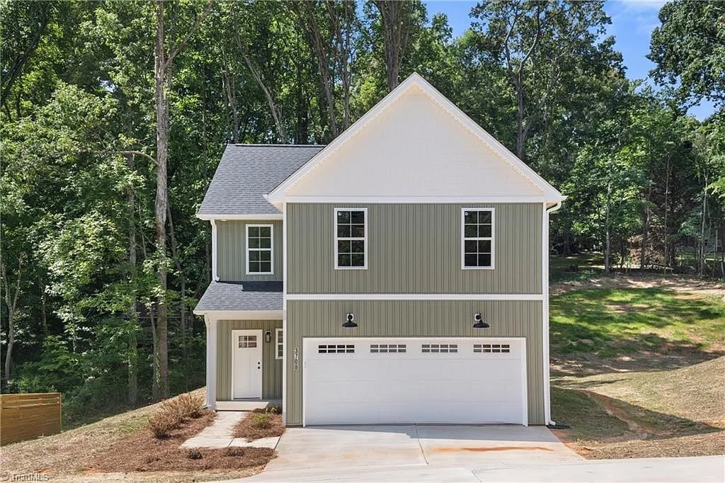 Modern two-story house with gray and white exterior, four-car garage, and pitched roof surrounded by mature trees