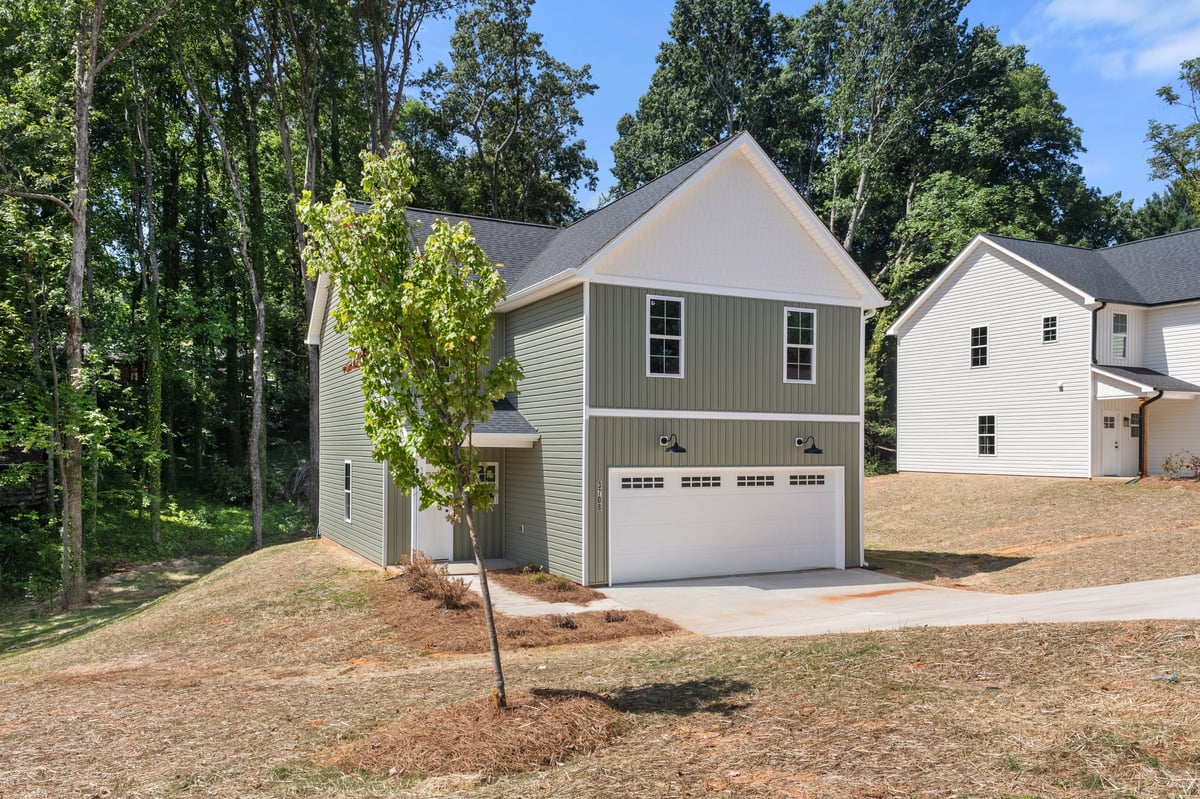 New two-story gray house with white garage doors surrounded by trees and landscaped yard