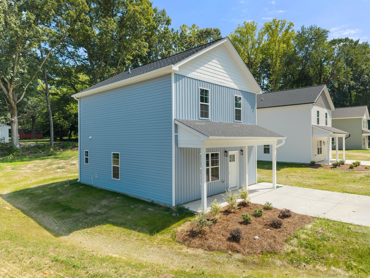 Light blue two-story house with white trim and porch, surrounded by green lawn and trees on a residential street