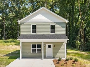 Two-story beige house with white trim, open garage, and front entrance surrounded by trees