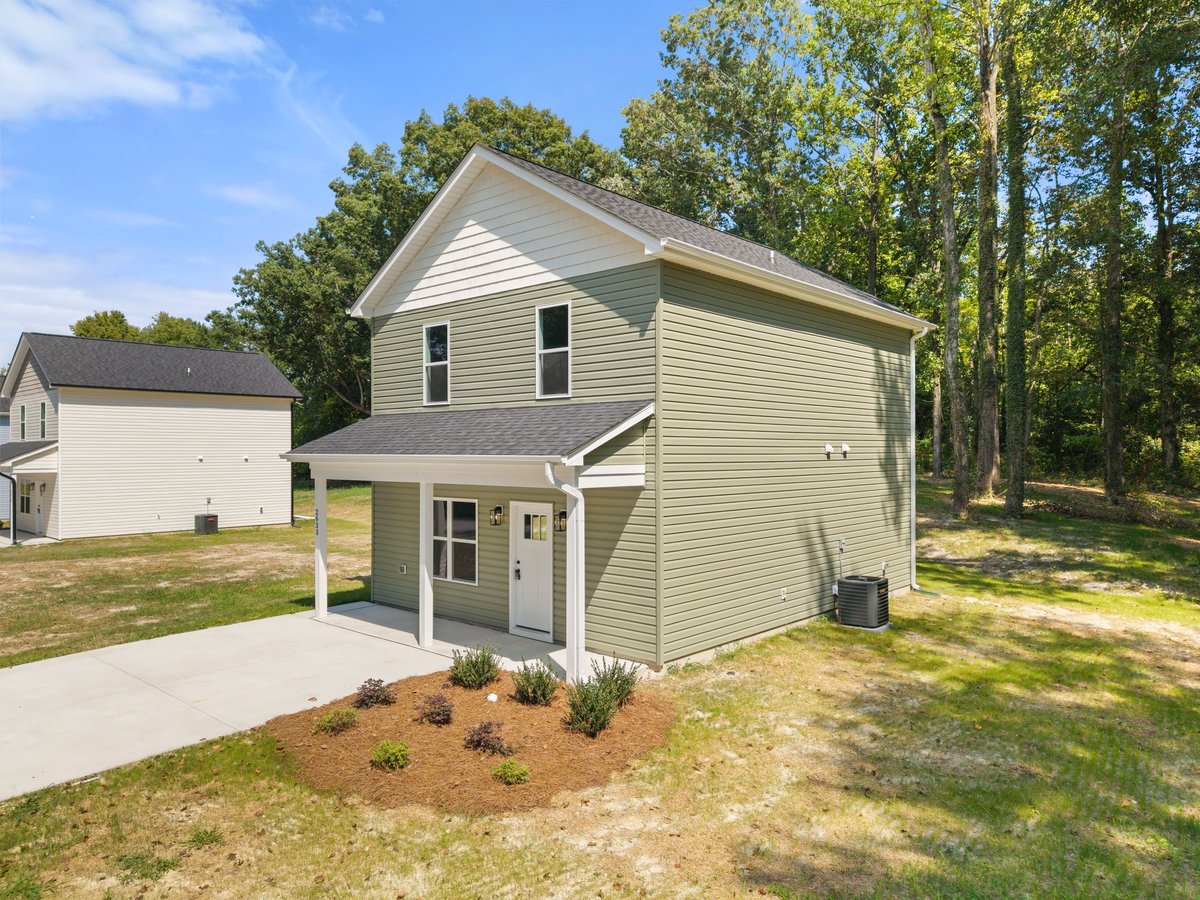 Two-story white vinyl house with covered porch and detached garage on a tree-lined lot