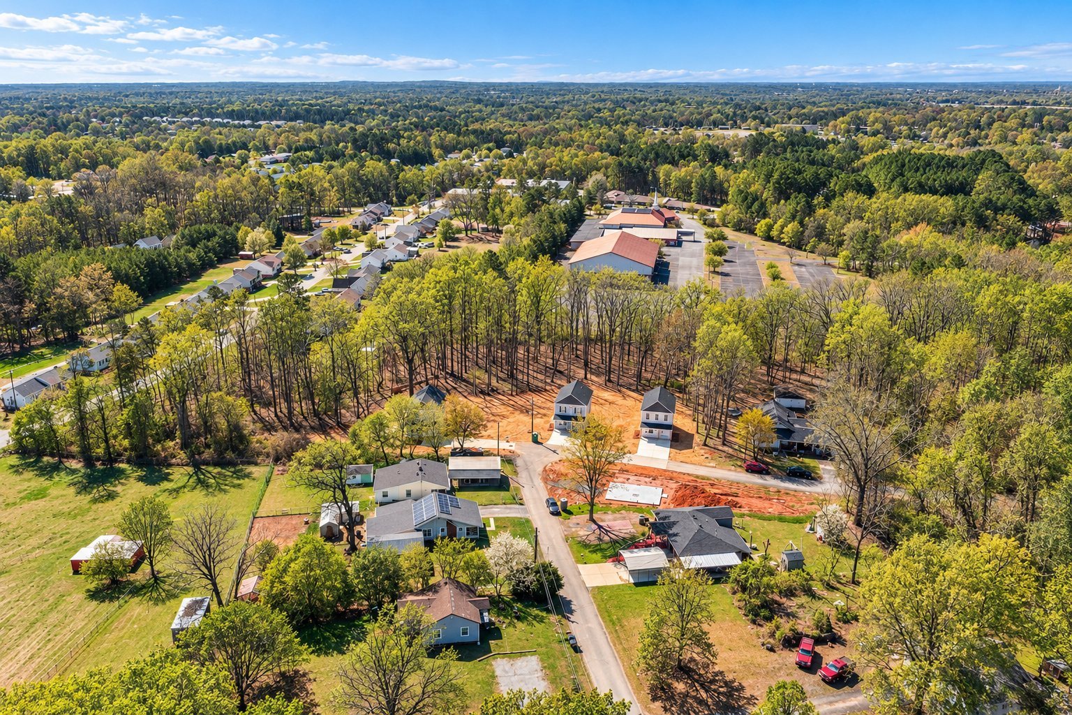 Aerial view of a residential suburban area with houses, trees, and parking lots surrounded by green woodland landscape