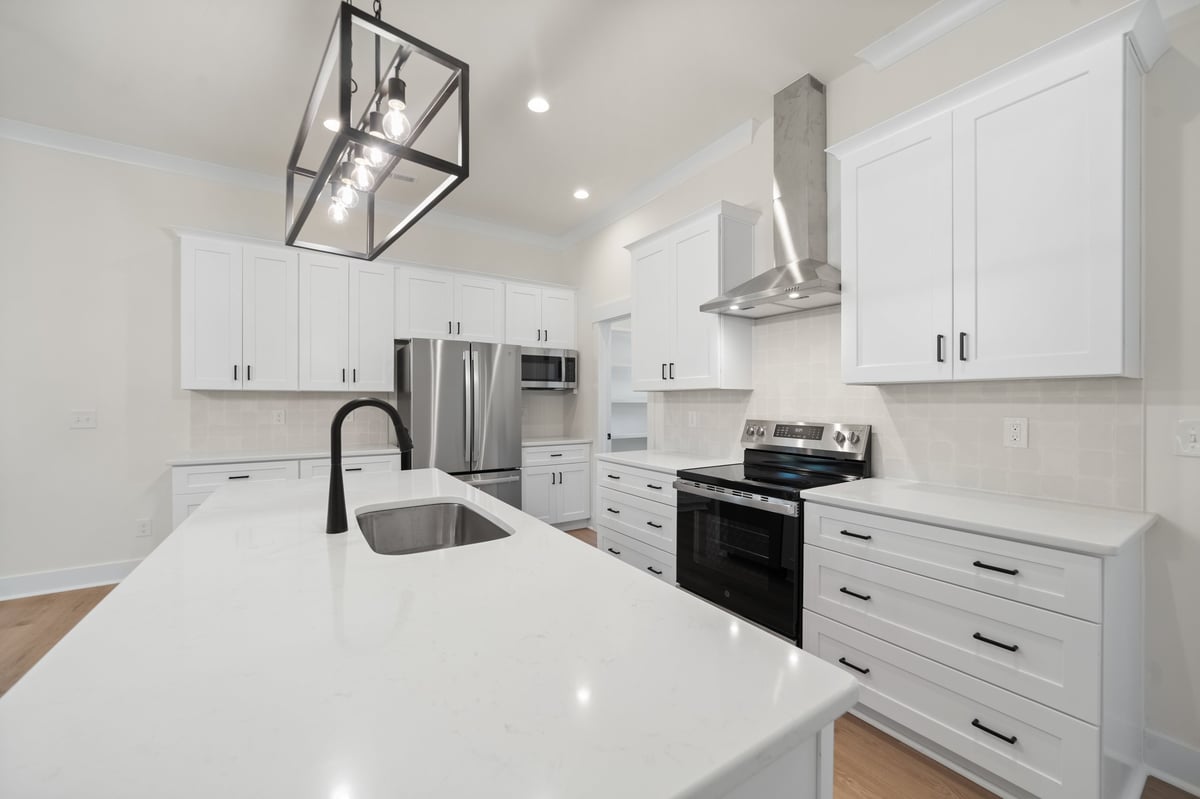 Modern white kitchen with white cabinetry, stainless steel appliances, white countertops, and island with sink
