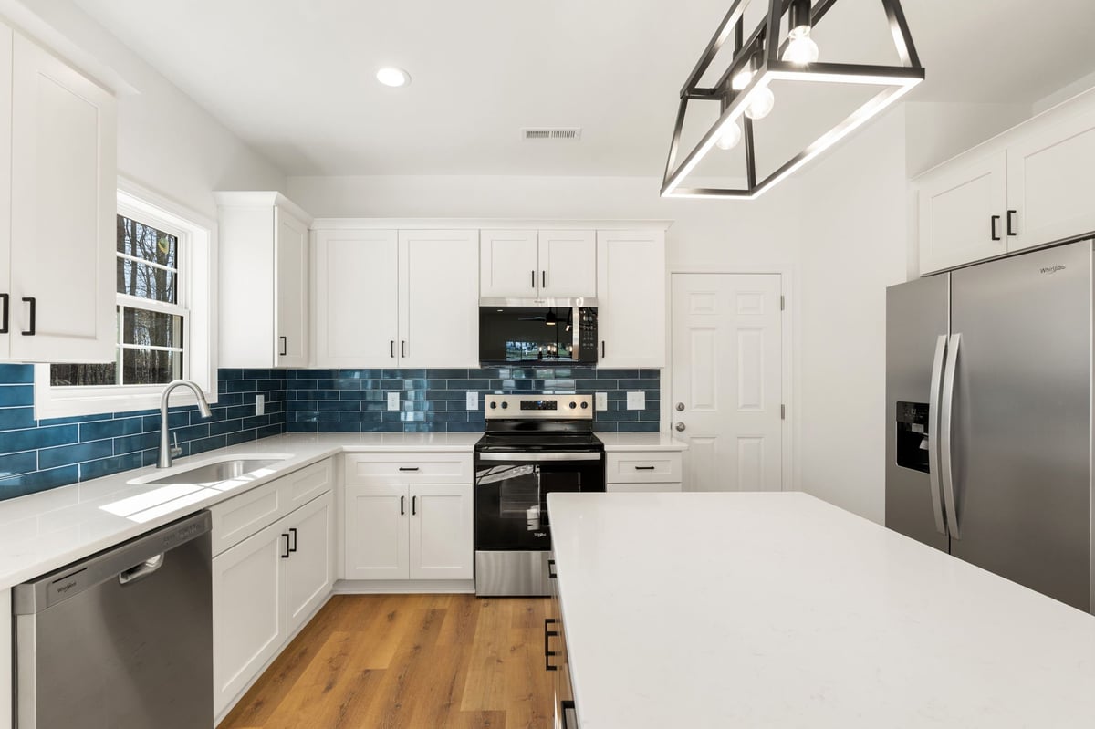 Modern white kitchen with stainless steel appliances, blue subway tile backsplash, white island, and hardwood flooring