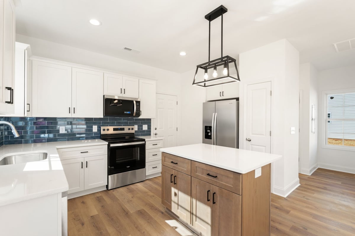 Modern kitchen with white cabinets, blue subway tile backsplash, stainless steel appliances, wood island with pendant lighting, and hardwood flooring.