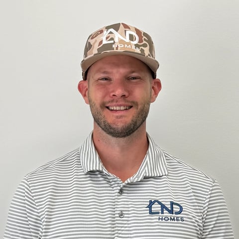 Man with beard wearing tan camouflage cap and striped polo shirt with AD Homes logo, smiling at camera