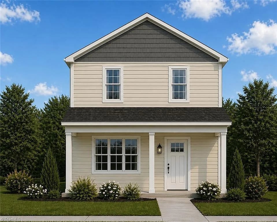 Two-story white farmhouse with black roof, front porch, white door, and landscaped garden on a sunny day