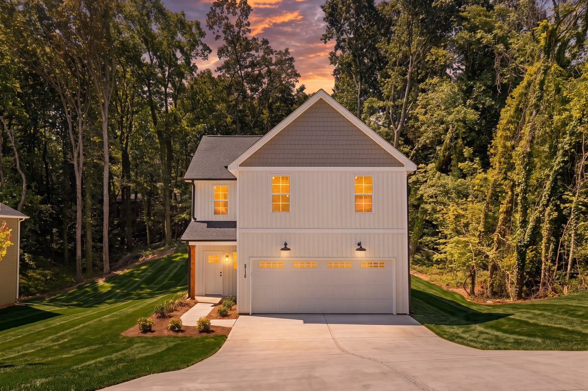 Modern two-story white house with garage at sunset, surrounded by tall trees and manicured lawn